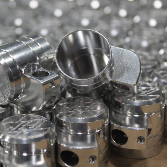 Batch of precision CNC-milled aluminum components with Dynacut logo stacked for inspection at Dynacut Manufacturing Quote about